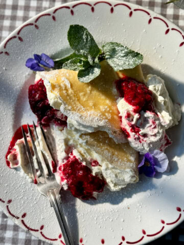 berry crepes on plate with raspberries and whipped cream.