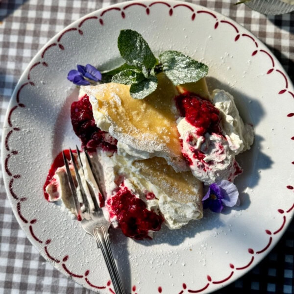 berry crepes on plate with raspberries and whipped cream.