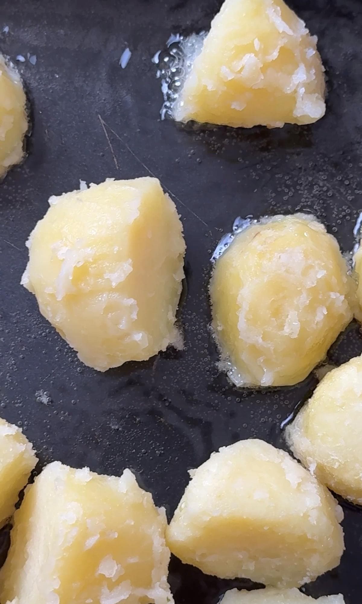 tipping parboiled potatoes onto hot oil.